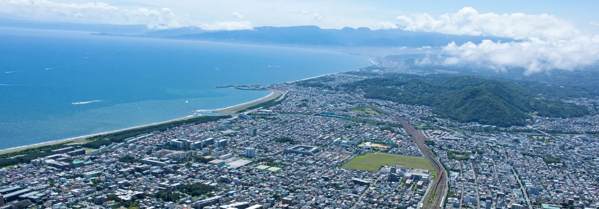 神奈川県平塚市の街並みと海岸線を望む空撮写真。広がる市街地と青い海が見渡せる景色。